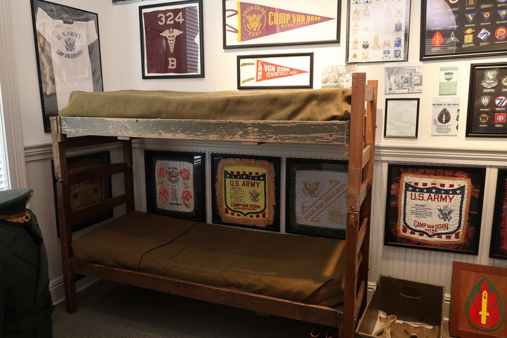 A WW2 museum display featuring bunk beds from the camp, surrounded by framed uniforms, pennants, and more.