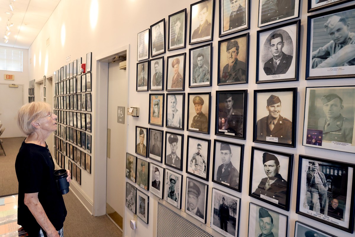 A woman stands in front of a WW2 museum display covered in framed portraits of soldiers in uniform
