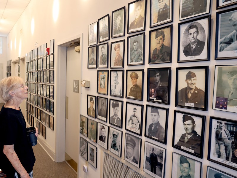 A woman stands in front of a WW2 museum display covered in framed portraits of soldiers in uniform
