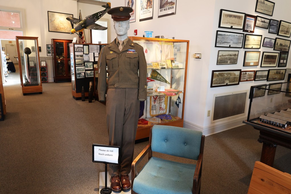 A WW2 museum display featuring A mannequin wearing a military uniform. Behind it are many displays on the walls