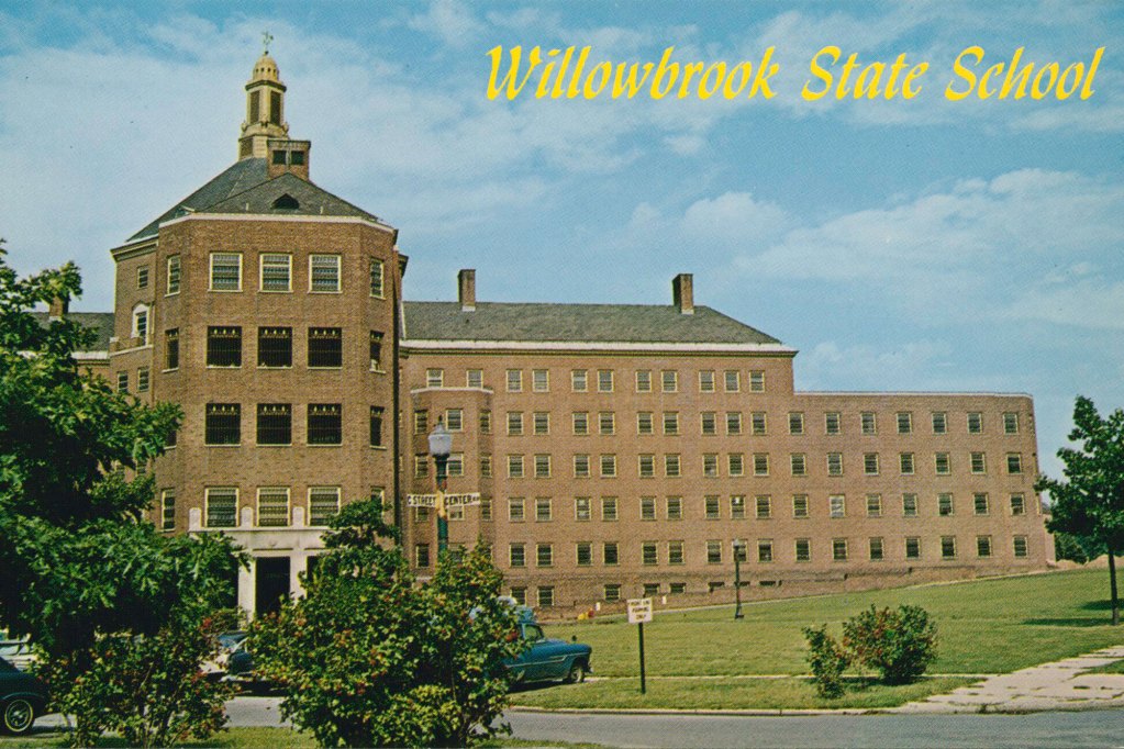A postcard of a state school building with a blue sky in the background trees in the foreground