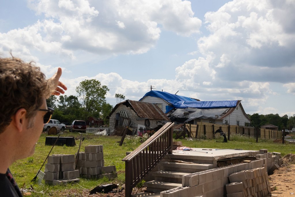 A man looking out a house in the distance with a blue covering on the roof
