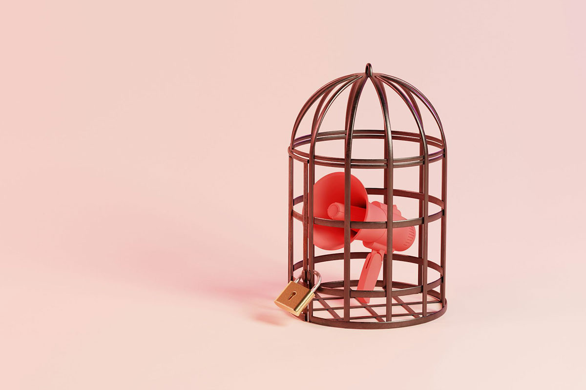 A locked birdcage contains a megaphone against a light red background