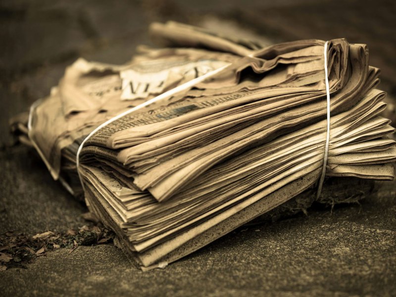 A stack of bound newspapers sit on concrete, left to the elements