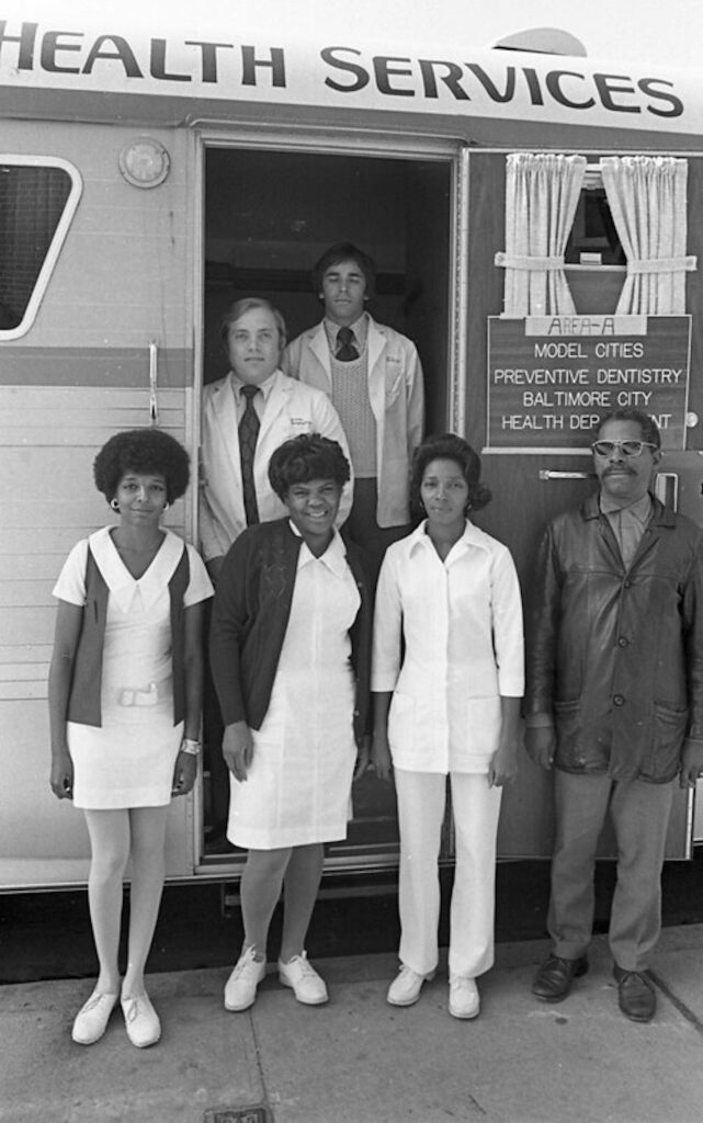 Six people pose next to a mobile health facility