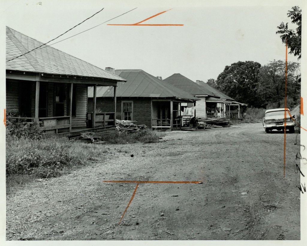 Black and white photo of old, one-story homes along a dirt road