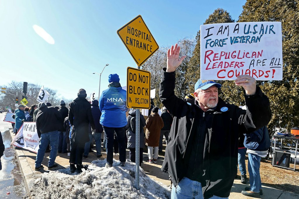 A man standing with a sign that says 'I'm a USAIR Force veteran Republican leaders are all cowards!'