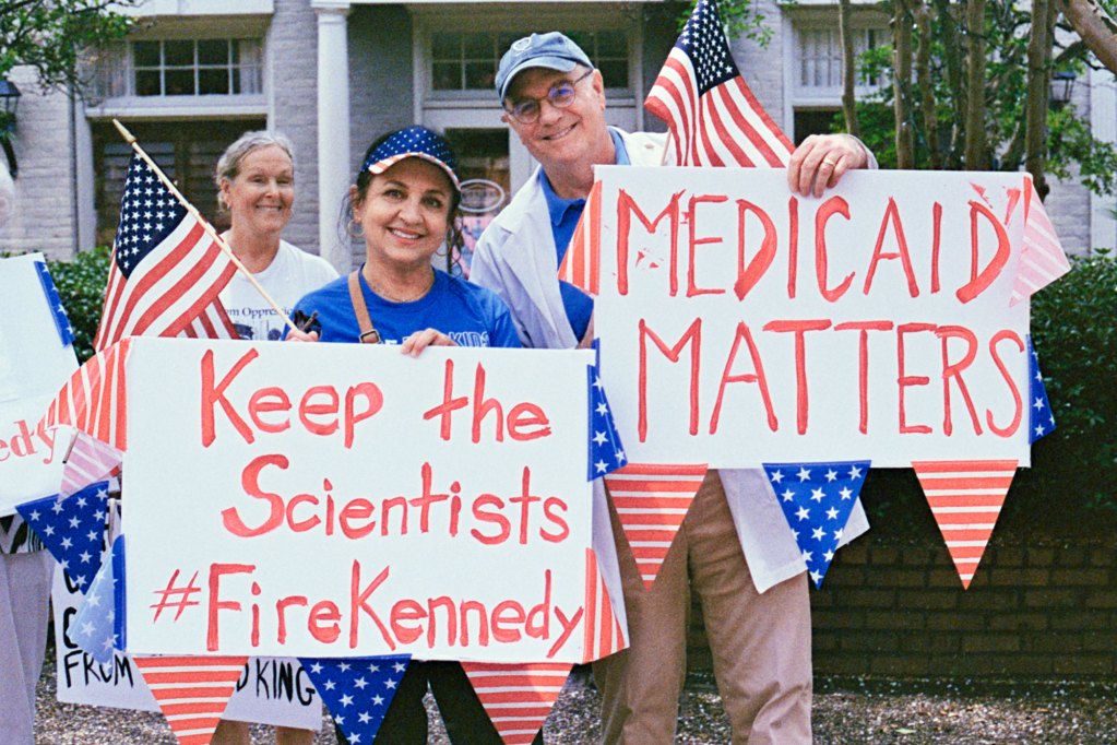 Protesters hold signs that read "Keep the scientists #FireKennedy" and "Medicaid Matters"