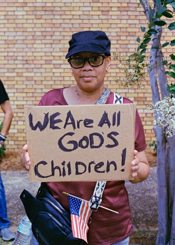 A protester holding a sign that reads "We are all God's children!"