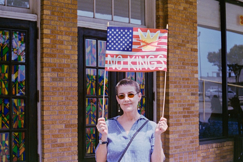 A protester holds a sign that reads "No Kings" on a US flag