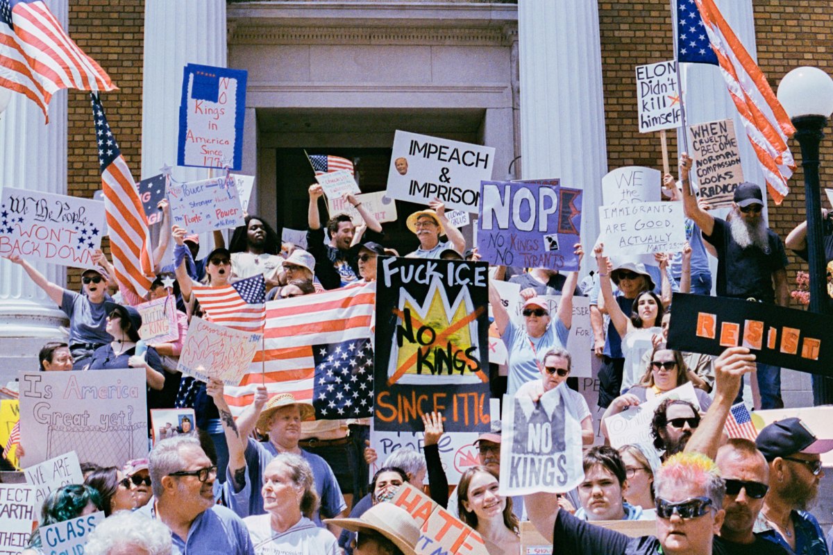 A large crowd of protesters hold signs that read things like "Impeach and Imprison" and "No kings"