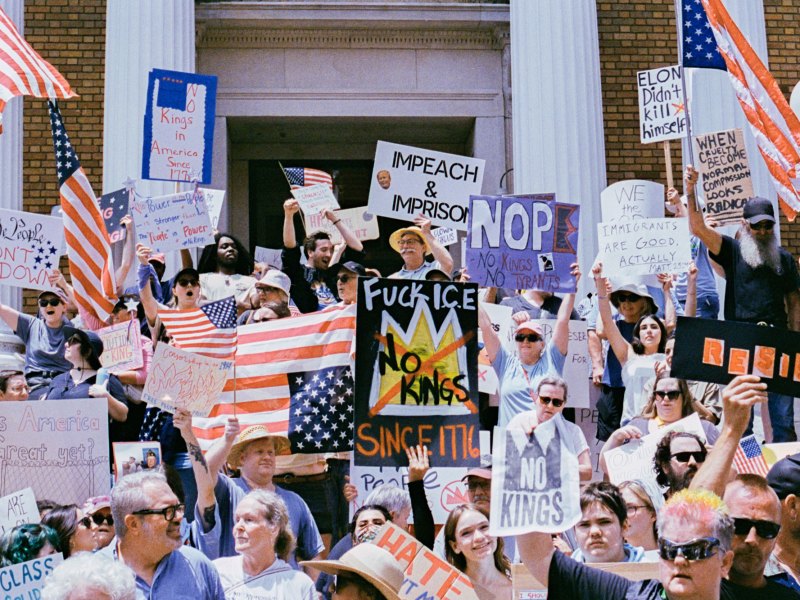 A large crowd of protesters hold signs that read things like "Impeach and Imprison" and "No kings"