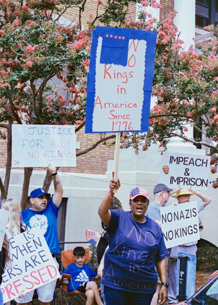 Protesters hold signs that say "No kings in America since 1776 and "No nazis no kings"