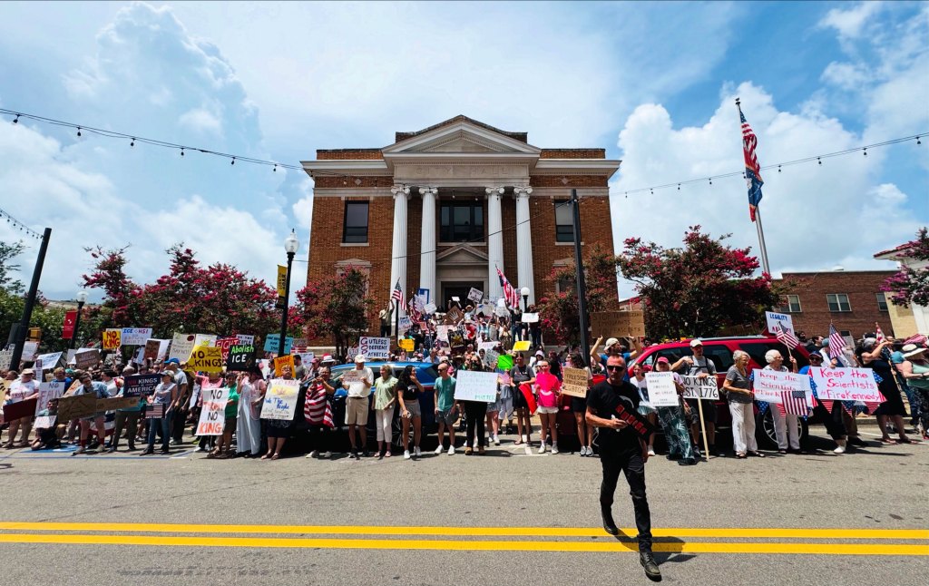 A wide view of protesters holding signs outside of a City Hall building