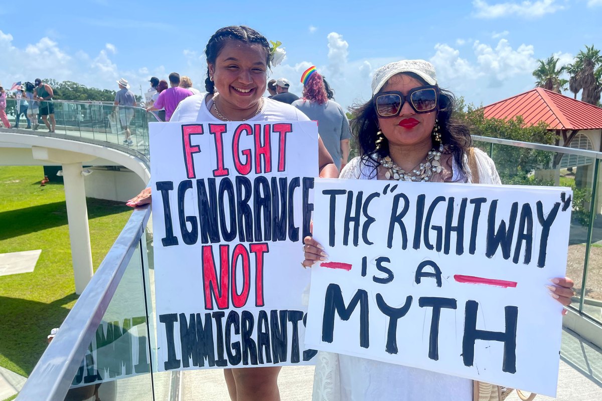 Two protesters hold signs on a bridge. They read "Fight Ignorance Not Immigrants" and "The 'right way' is a myth"