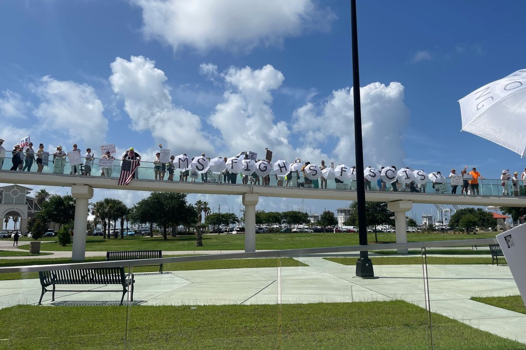 Protesters hold up signs on a bridge, spelling "MS Fights Fascists" on white umbrellas"
