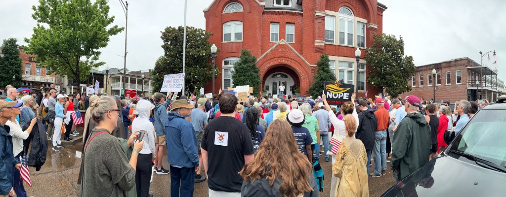 A panoramic view of protesters gathered outside holding up signs