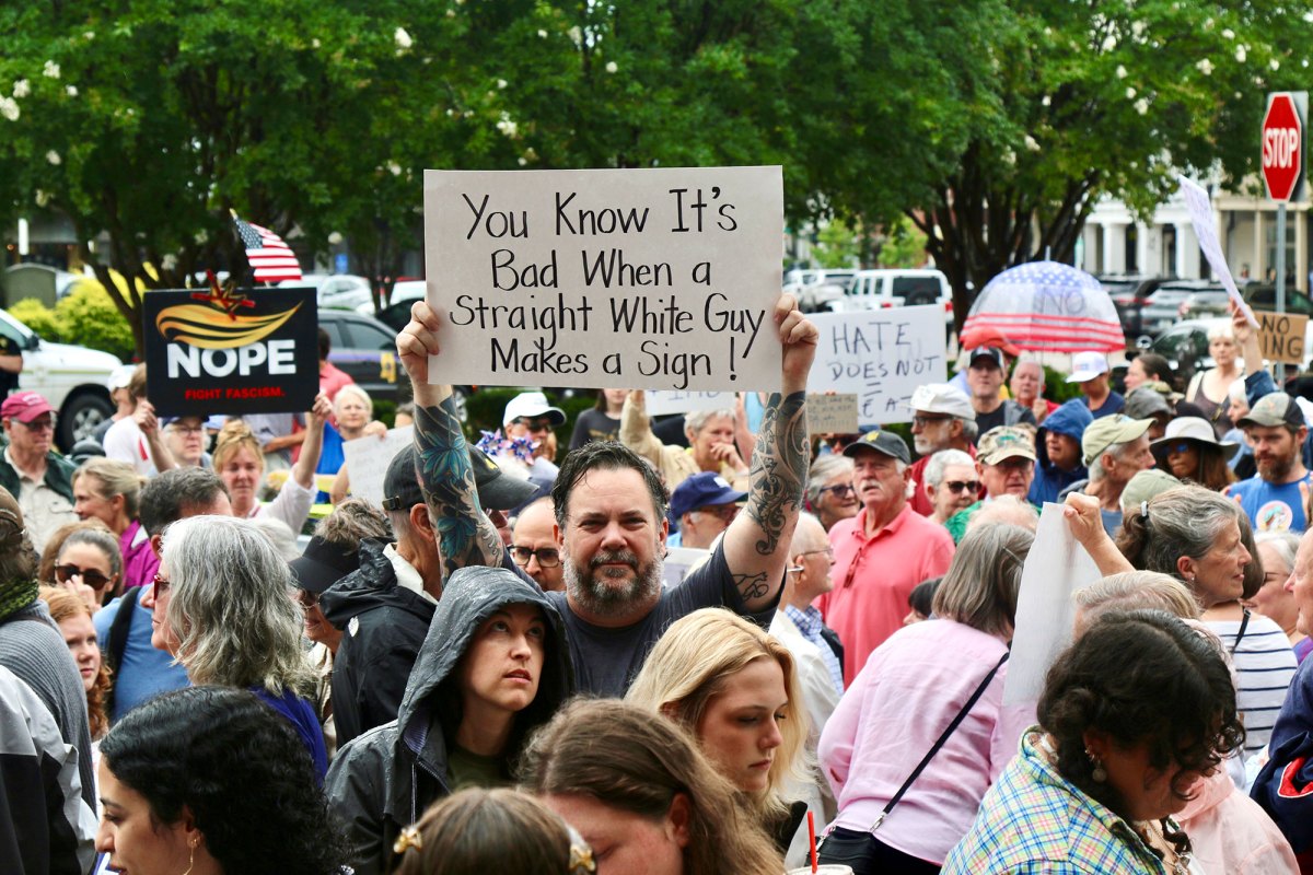 A crowd of protesters carry signs, one reads "You know it's bad when a straight white guy makes a sign!"