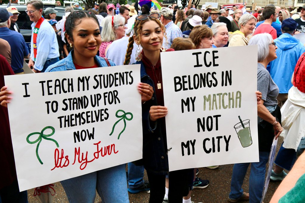 A crowd of protesters carry signs, one reads "I teach my students to stand up for themselves, now it's mu turn" and "Ice belongs in my matcha not my city"