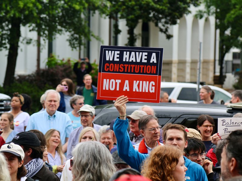 Protesters outside holding signs, one reads "We have a constitution, not a king"
