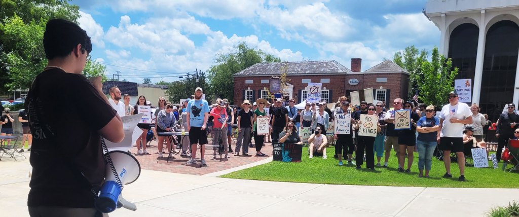 Protesters hold up signs as one person in the foreground organizes them