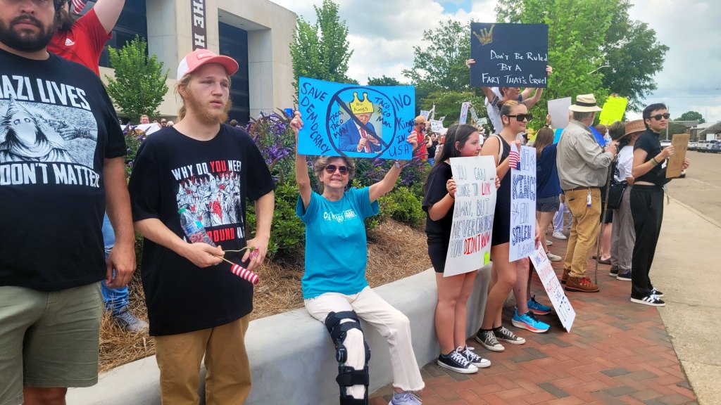 Protesters hold up signs, one reads "Save democracy! No Kings in USA"