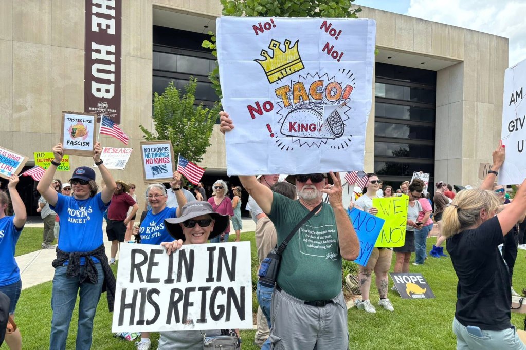 Protesters hold up signs, one reads "No! no! no! no! taco! king!" and another reads "Rein in his reign"