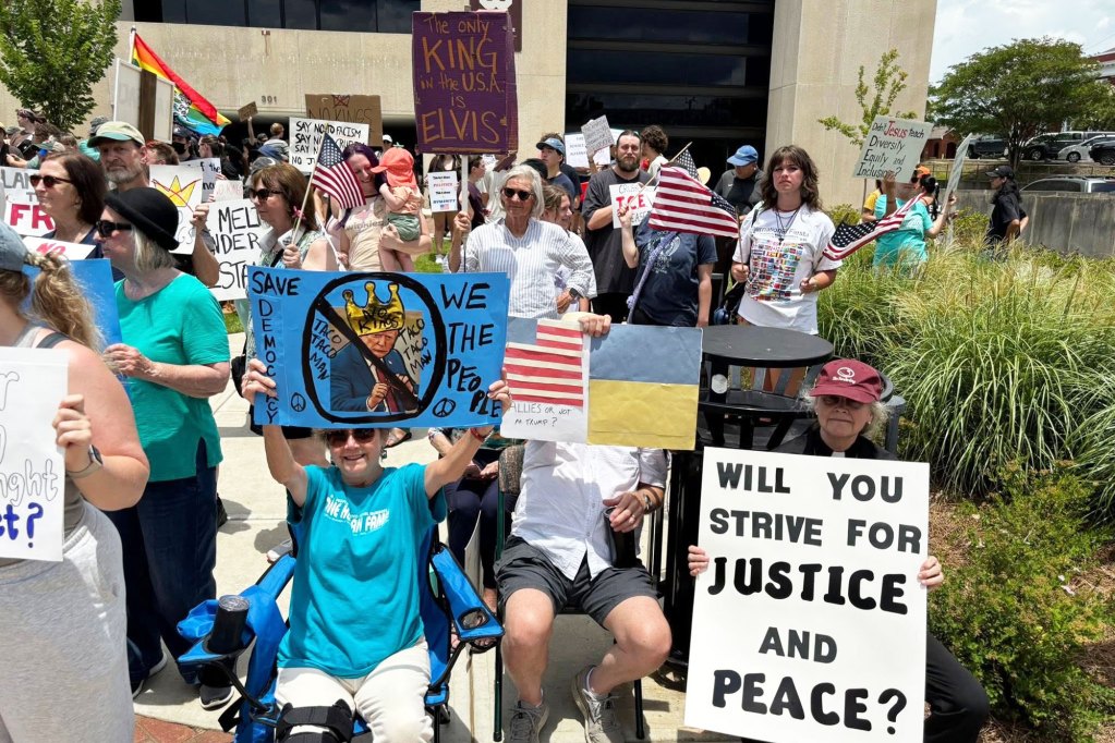 Protesters hold up signs, one reads "Will you strive for Justice and Peace?"