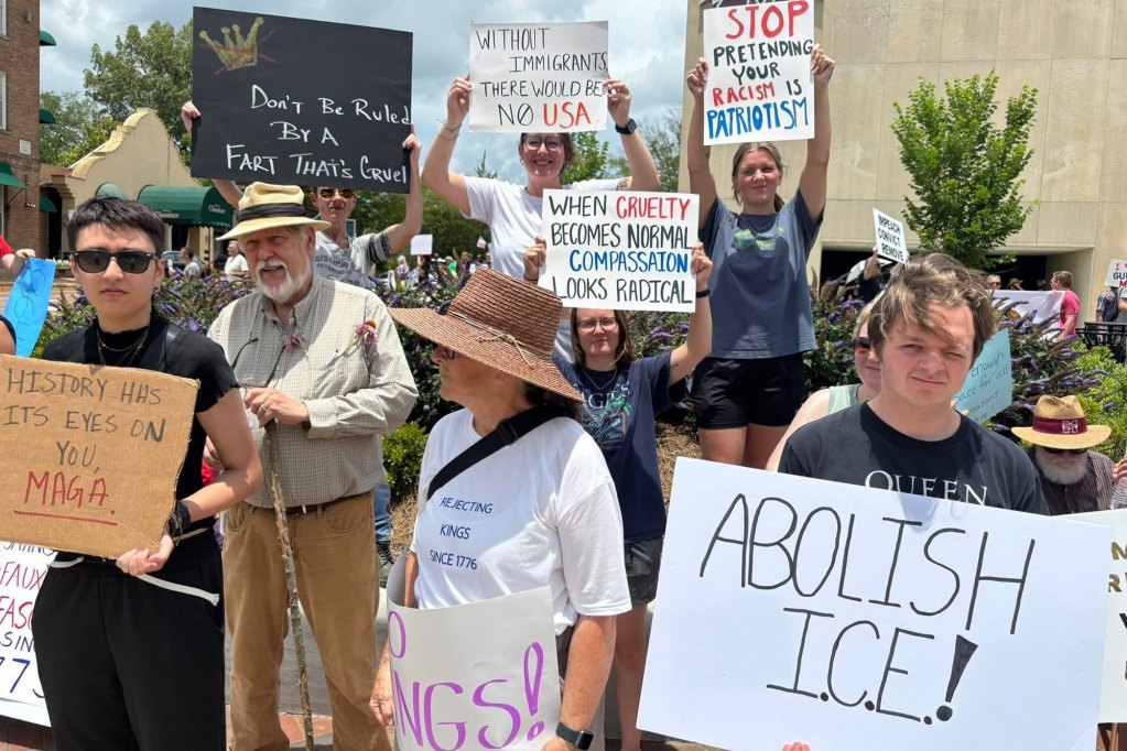 Protesters hold up signs, one reads "Stop pretending your racism is patriotism"