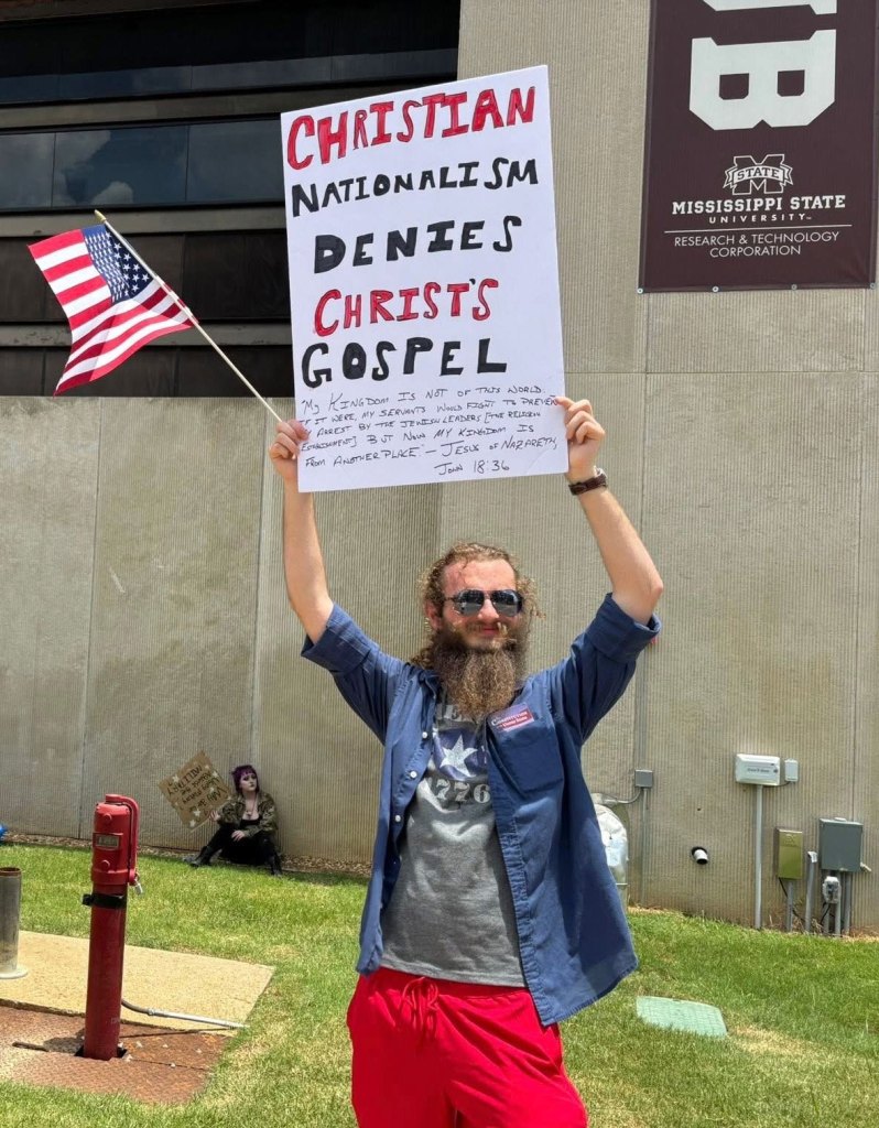 Protesters hold up signs, one reads "Christian nationalism denies Christ's gospel"