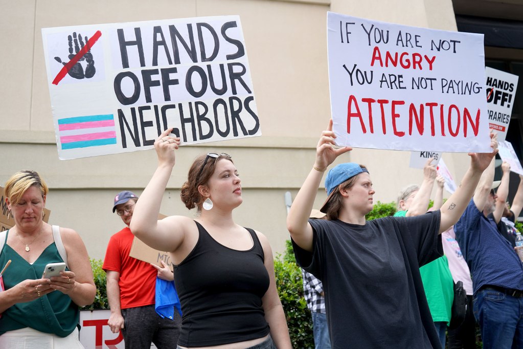 A crowd of protesters carry signs, one reads "If you are not angry you are not paying attention"