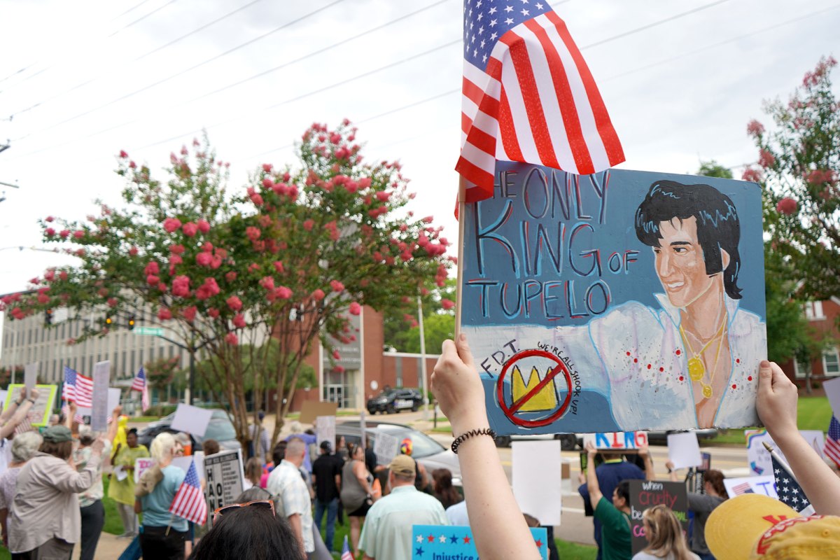 A crowd of protesters carry signs, one reads "Only king of Tupelo" with a painting of Elvis
