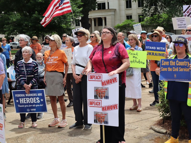 A crowd of protesters standing with signs that read things like "Save the Country, Save the Civil Service" and "Impeach, Remove"