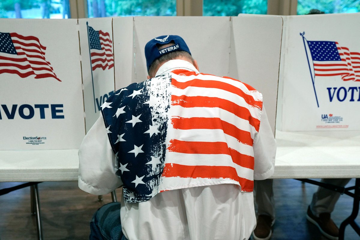 The rear view of a man in a veteran cap and US Flag top sitting at a row of voting paritions