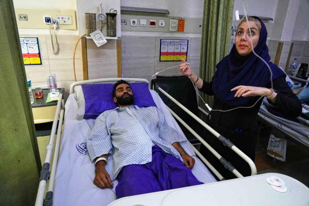 a nurse checks the IV of a. man in a hospital bed