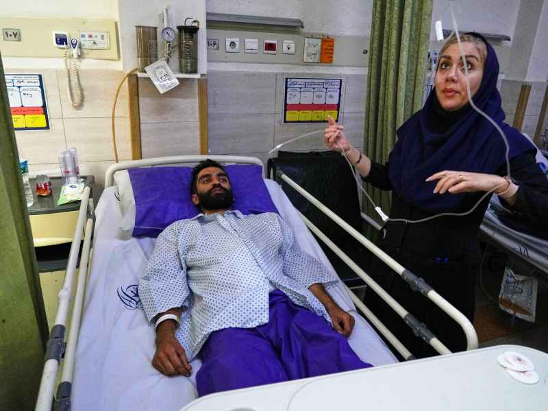 a nurse checks the IV of a. man in a hospital bed