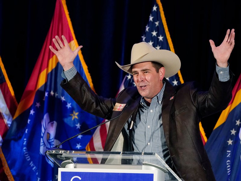 Andy Gipson in trademark cowboy hat, raised hands smiling on stage in front of US and Mississippi state flags