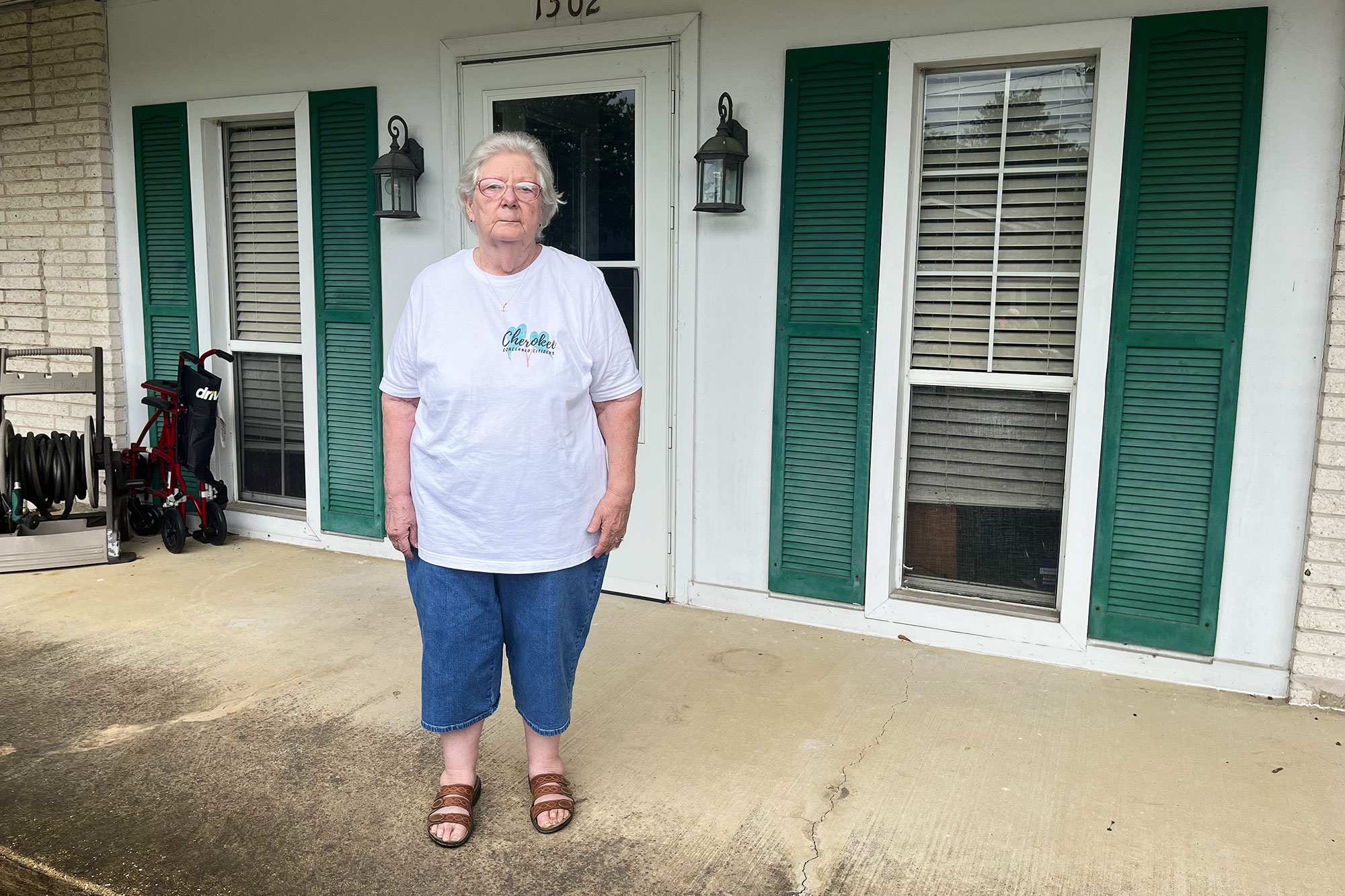 A woman is seen standing on the porch of a white building with green shutters
