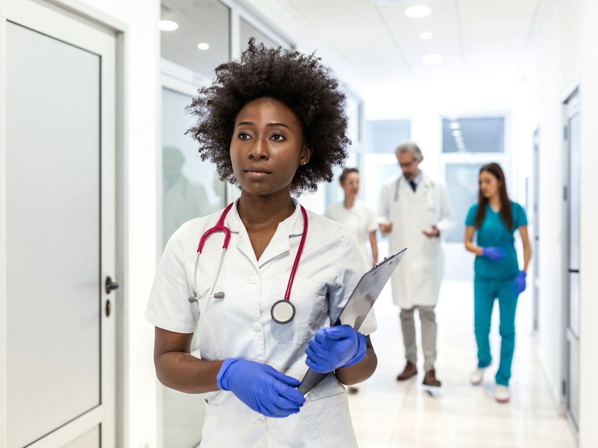 Woman with black hair in a white coat with blue gloves on her hands