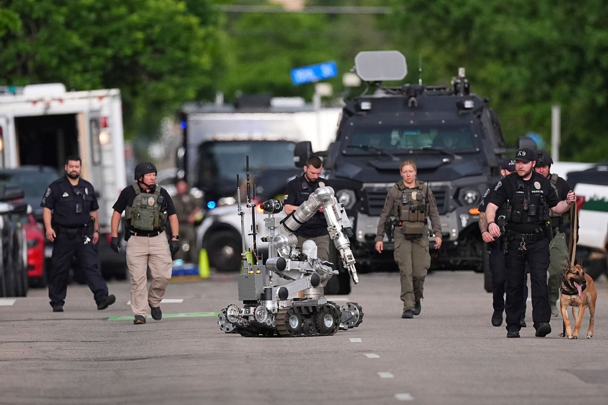 A row of police walk down a street with a police dog and a bomb robot in tow