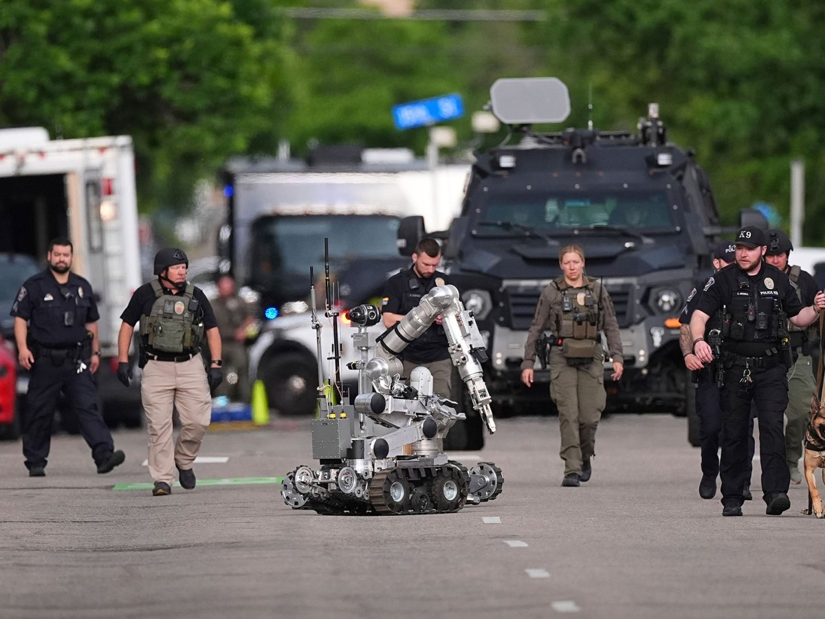 A row of police walk down a street with a police dog and a bomb robot in tow