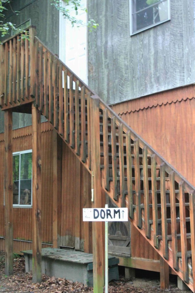 Wooden stairs on the side of a two story building, with a handwritten white sign in front that reads DORM