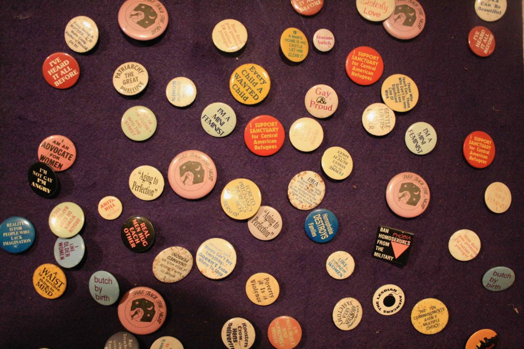 A board full of small circular canned pins with text like "I'm a mini feminist" and "I am an advocate for Women"