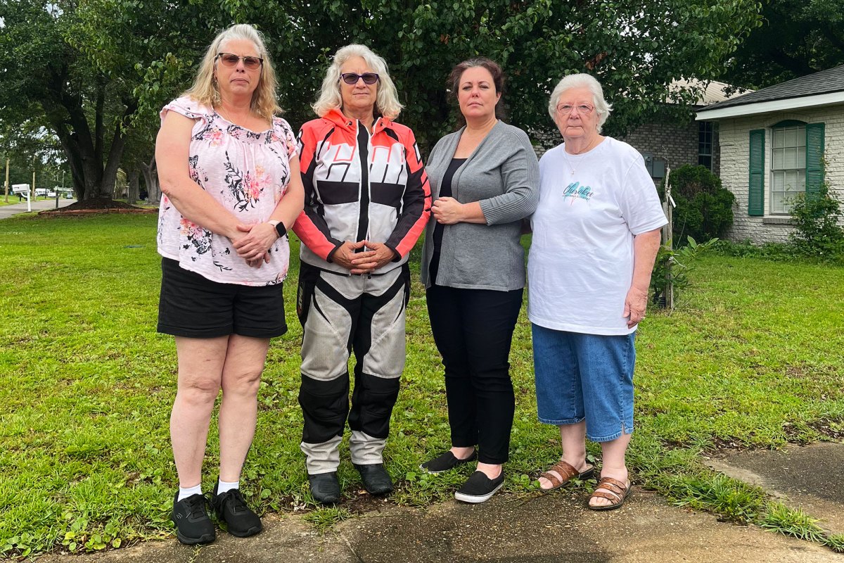 Four women stand side by side along the edge of a front yard driveway