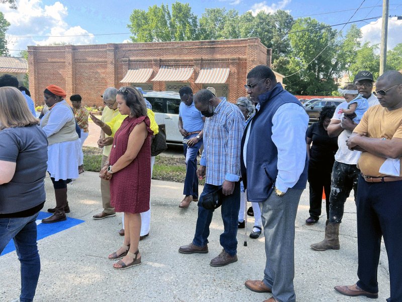 Many community members stand outside with heads down in prayer