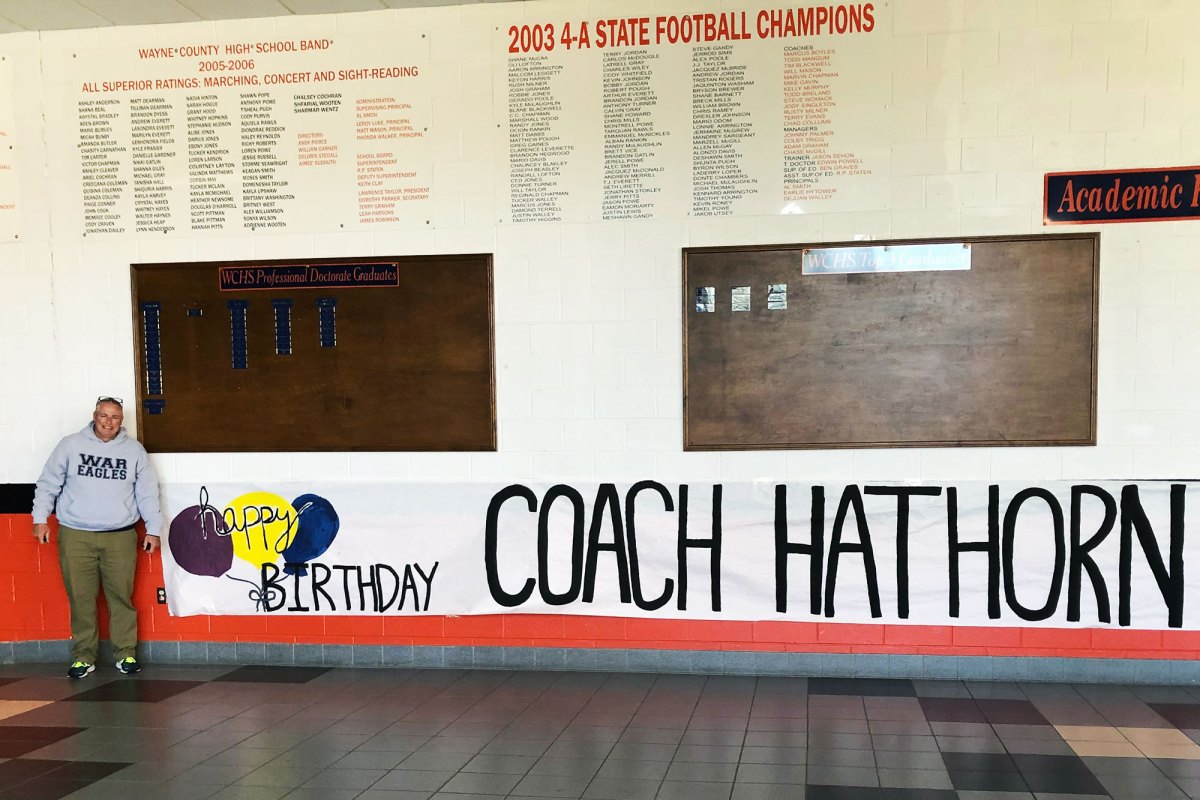 A man poses by a sign that reads Happy Birthday Coach Hathorn