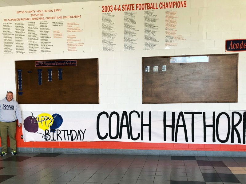 A man poses by a sign that reads Happy Birthday Coach Hathorn