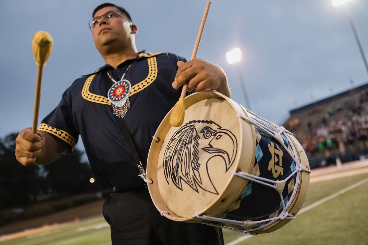 Cyrus Ben playing a traditional Choctaw drum on a football field