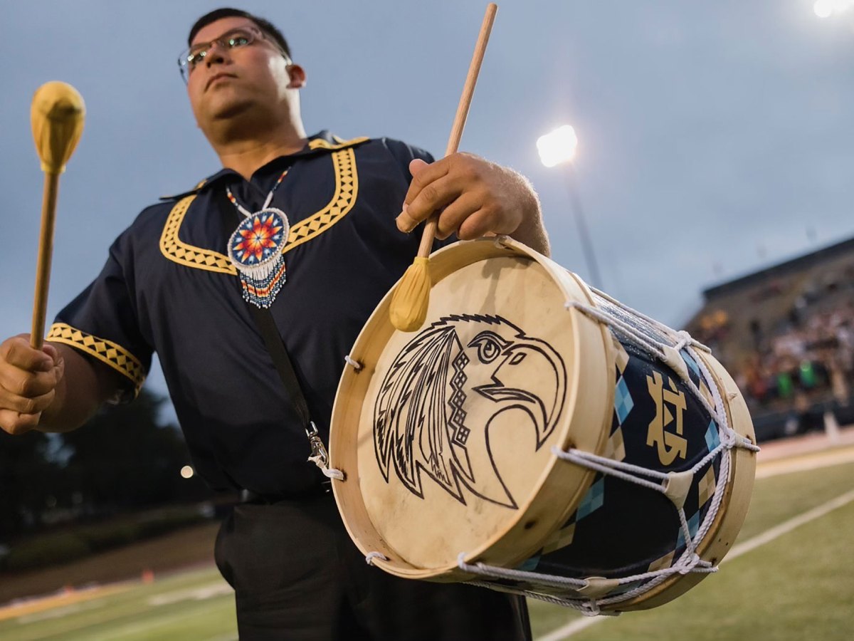 Cyrus Ben playing a traditional Choctaw drum on a football field