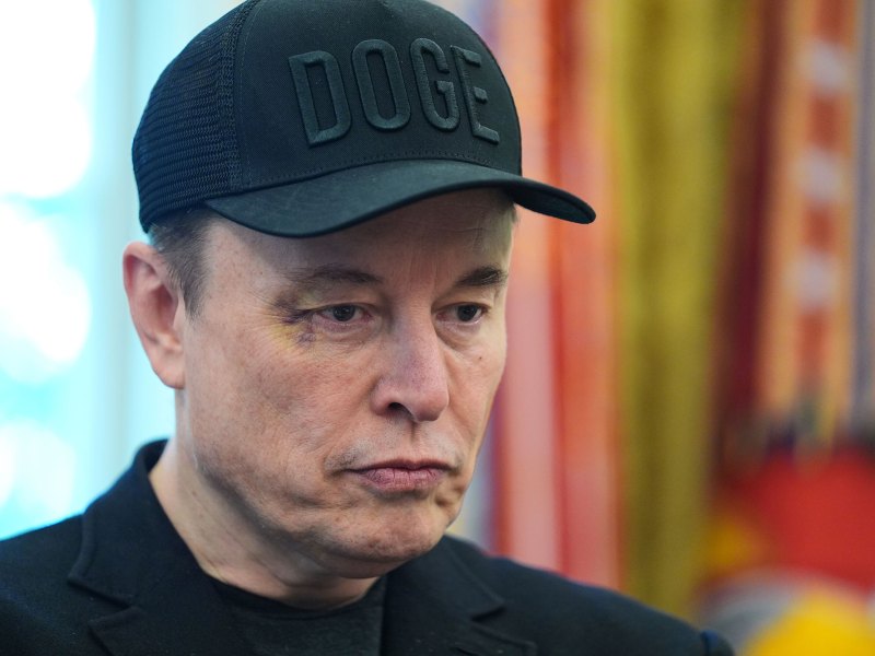 A closeup of Elon Musk in the White House, wearing a black DOGE cap and sporting a black eye